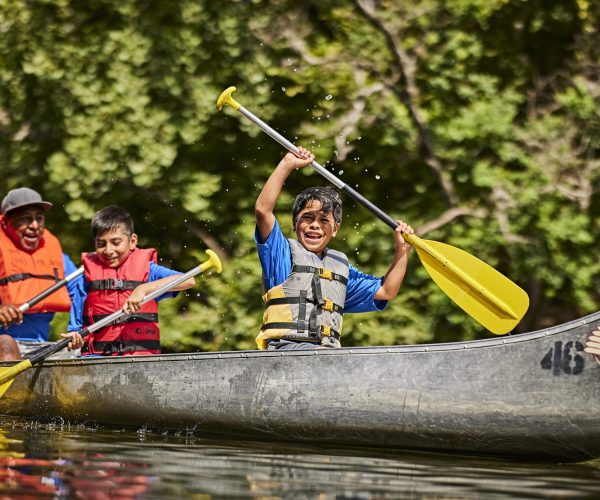 Cub Scouts paddling a canoe with dad; rowing on a river; excited; excitement