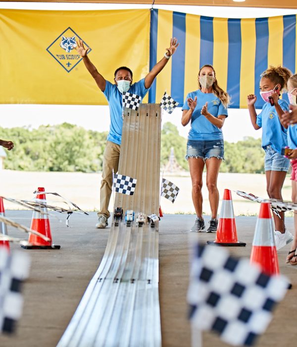 Cub Scouts racing cars on a Pinewood Derby track wearing masks at a park pavilion